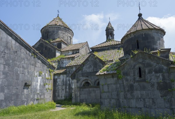 Impressive stone church towers with decorative details under blue skies and green vegetation,