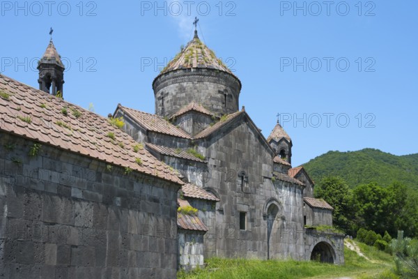 Old monastery building with stone structures and dome in front of a green mountain landscape,
