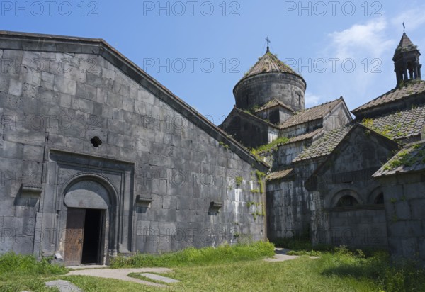 Massive stone church with large windows and an open wooden gate under a blue sky, Haghpat