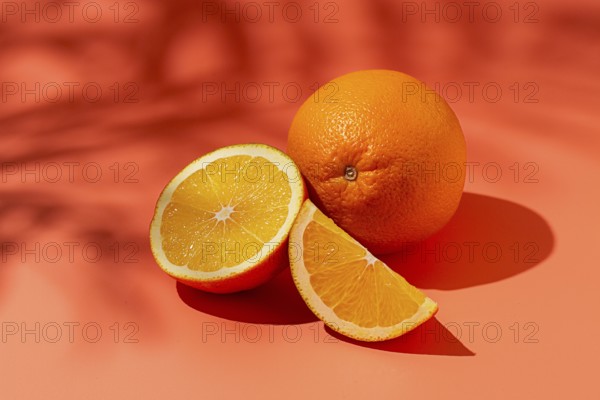 On the coral surface, next to two neatly sliced slices, there is a whole orange. Sunlight casts