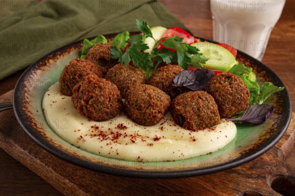 A plate holds falafel balls, tahini, salad with tomatoes and cucumbers, and a drink. The setting is