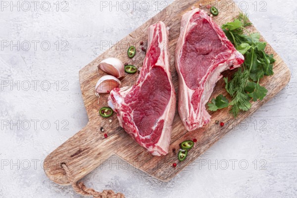 Fresh pieces of beef on the bone, on a wooden cutting board, with herbs and spices, ready for