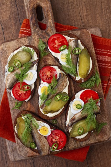 Sandwiches on rye bread with sprats, quail eggs, fresh tomatoes and pickled cucumber, on a wooden