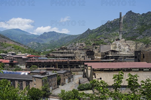 Industrial plant in a mountainous area with old buildings and chimney surrounded by green hills,