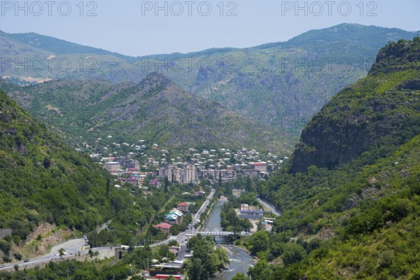 Mountain landscape with a town in the valley surrounded by lush greenery and a river flowing