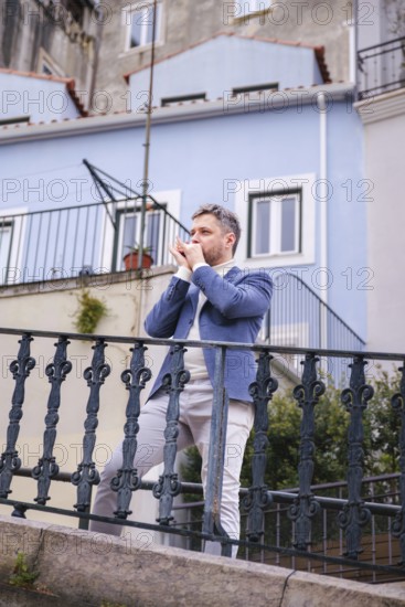 Man musician in a blue blazer and white sweater playing blues on a harmonica with eyes closed,