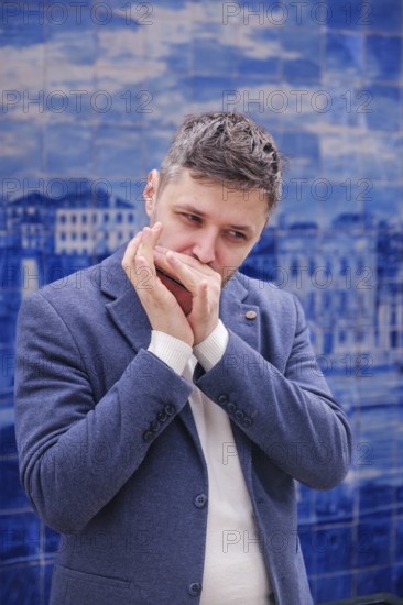 Man musician in a blue blazer and white sweater playing blues on a harmonica with eyes closed,