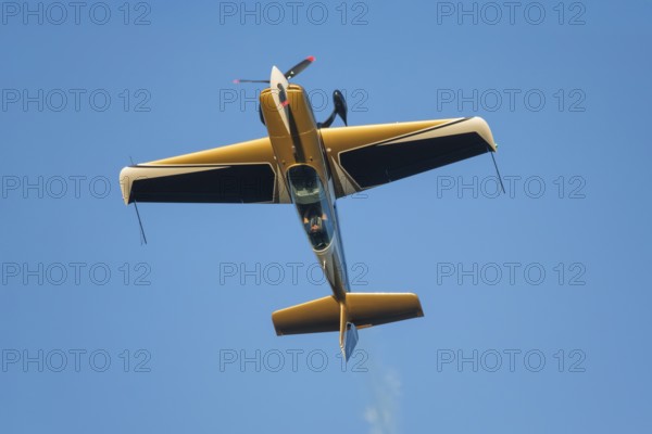 Golden stunt aerobatic plane performing stunts in blue sky. Concept of speed, difficulty,