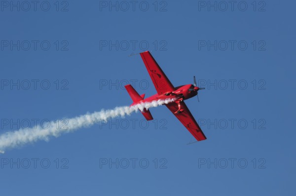 Red stunt aerobatic plane performing stunts in blue sky. Concept of speed, difficulty, precision,