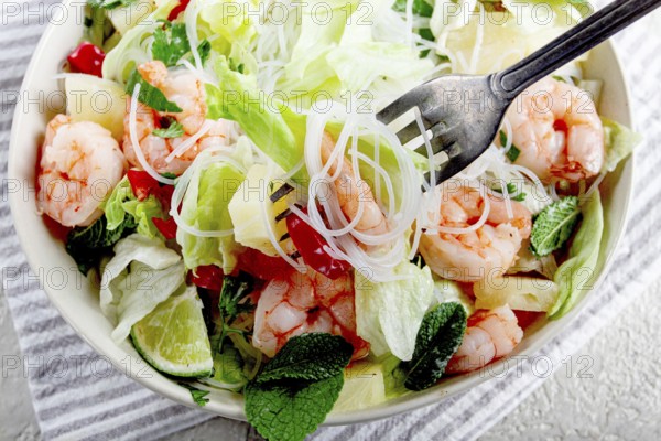 Thai salad with shrimp and rice noodles, pineapple slices, coriander and mint leaves, on a white