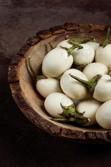 White mini eggplant, in a wooden bowl, on the table, close-up