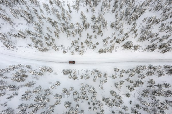 Aerial view over car, van driving over snow covered road through the taiga in winter, Riisitunturi