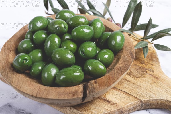 Halkidiki olives, classic Greek green olives, in a wooden bowl, on a cutting board, top view,