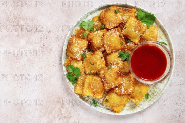 Fried ravioli with parmesan cheese, served with red sauce and garnished with herbs, on a light