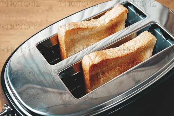 Two slices of bread are toasting in a shiny metal toaster, set on a countertop in a warm kitchen.