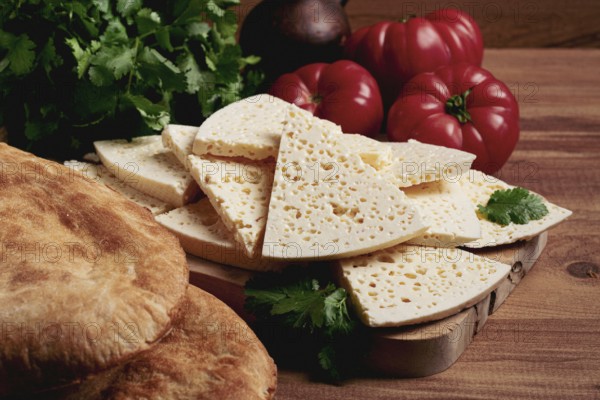 Georgian sliced cheese, on a wooden chopping board, with tomatoes with herbs and lavash, rustic