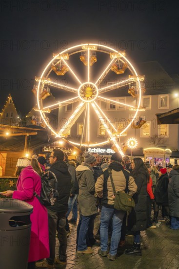 People gather in a Christmas square in front of an illuminated Ferris wheel, Christmas market 2025,