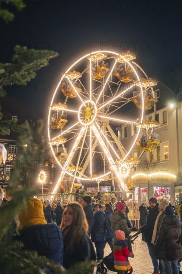 A brightly lit Ferris wheel rises above a crowd at a Christmas market, Christmas market 2025,