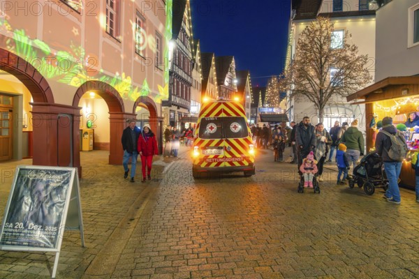 Busy Christmas market at night with rescue service vehicle and festive lighting, Christmas market