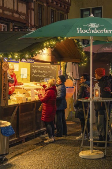 People stand at a well-lit stand to buy pastries at a Christmas market, Christmas market 2025,