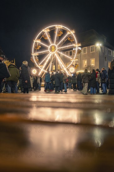 People enjoy the illuminated Ferris wheel on a cobblestone square at night, Christmas market 2025,