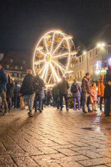 People walk across a square with illuminated Ferris wheel at night, Christmas market 2025, Nagold,