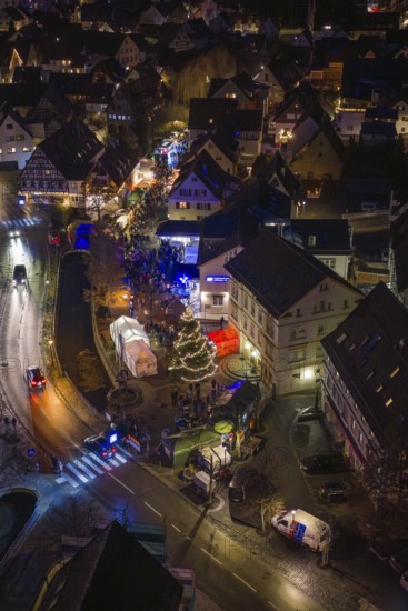 Aerial view of an illuminated Christmas market at night with a shiny Christmas tree and crowds of