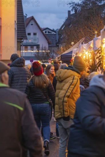 Visitors to a busy market stroll through festive lighting, Aidlingen Christmas Market, Böblingen