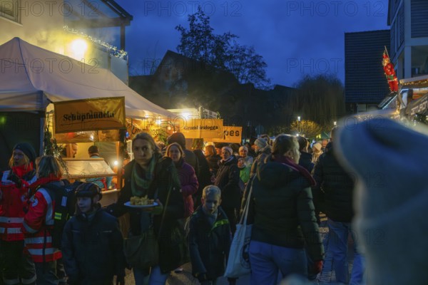 Families and children stroll through festively lit food stalls at a Christmas market in the