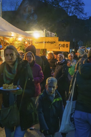 Crowd of people wait in front of an illuminated food stand at night, Aidlingen Christmas market,