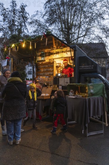An illuminated food truck at a street market with people in a nocturnal atmosphere, Aidlingen