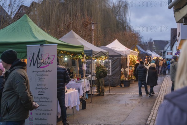 People stroll through a market with various illuminated stands in the evening, Aidlingen Christmas