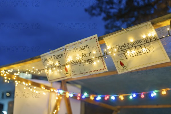 Glowing signs and fairy lights draw attention to a punch stand in the evening, Aidlingen Christmas
