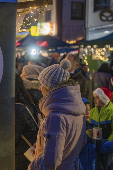 Woman in warm winter clothes holding coffee cup surrounded by children and twinkling lights at the