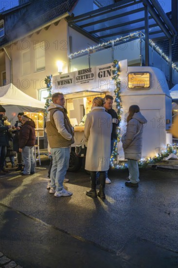 Friends chatting in front of an illuminated beverage stand at night, Aidlingen Christmas Market,