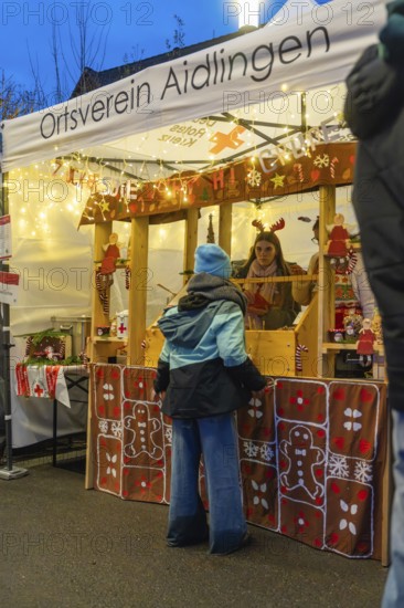 Christmas market stand with glowing decorations and people in front of it, Aidlingen Christmas