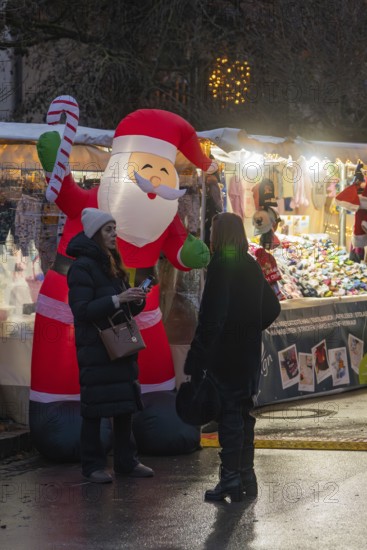 Two woman talking in front of an inflatable Santa Claus and an illuminated stand, Aidlingen