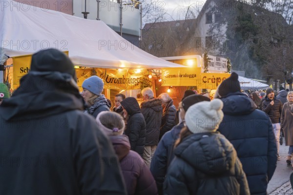 People wearing winter clothes in front of illuminated food stalls at a market, Aidlingen Christmas