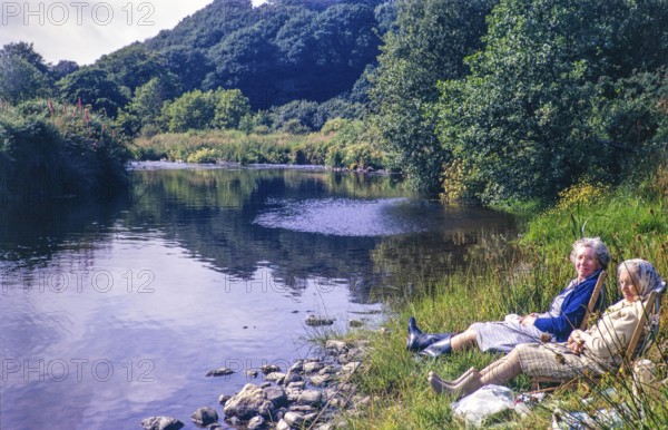 Two women sitting in deckchairs by the side of River Nevern, Penwaun, Nevern, Pembrokeshire, Wales,