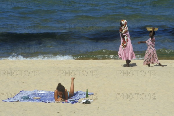 Tourist in bikini and traditionally dressed local woman at Kande Beach on Lake Malawi, Malawi,