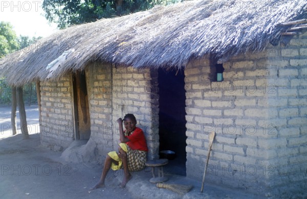 Woman sitting in front of a house in a village near Kande on Lake Malawi, Malawi, Africa, July