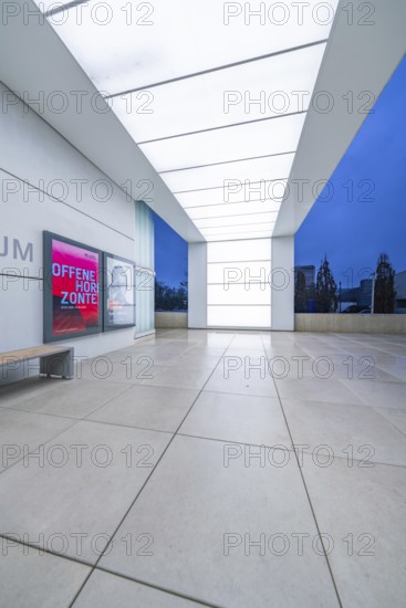 Modern museum entrance with blue lighting and large windows in the evening, Open Horizons
