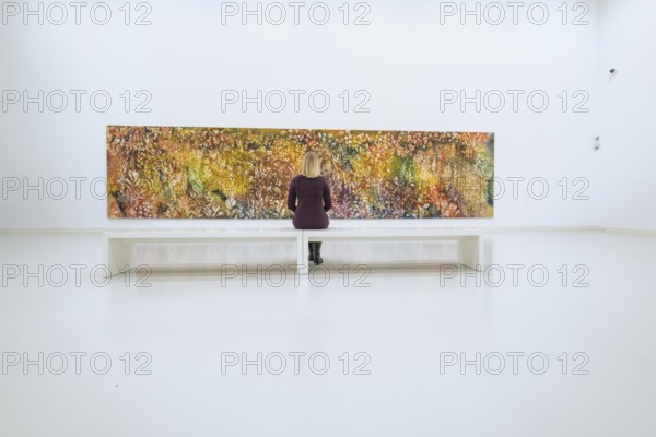 Woman sitting on bench looking at large, colorful, abstract work of art, Open Horizons exhibition,