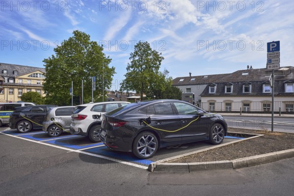 Parking lot, electric car, e-car with charging cable, general architecture, trees, blue sky,