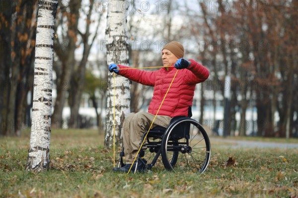A man in a red jacket and beige hat performs strength training using resistance bands while seated