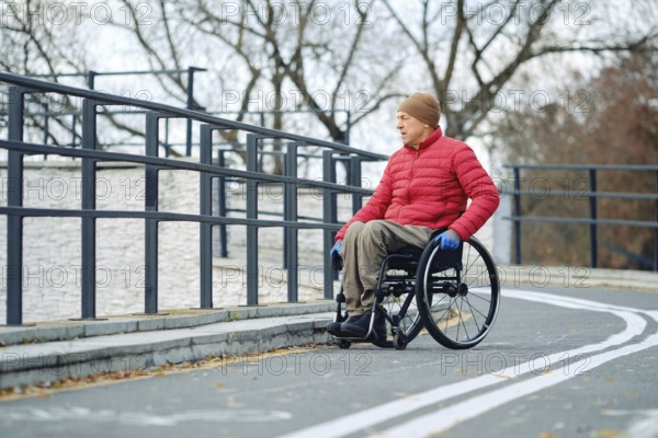 A senior man wearing a red jacket and hat is moving in his wheelchair along a smooth, winding path