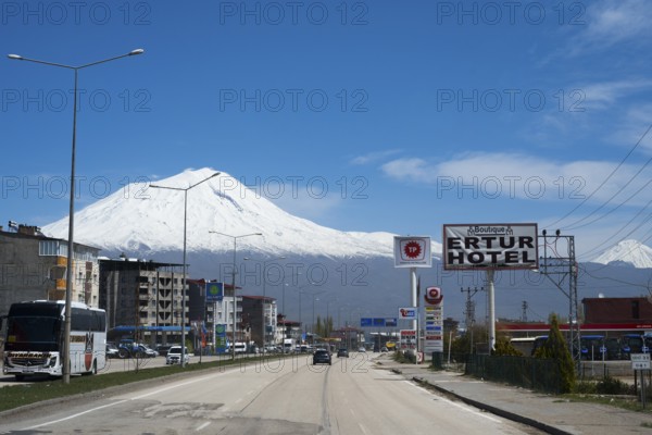 Road with passing vehicles flanked by a hotel and snow-capped mountains in the background, Great