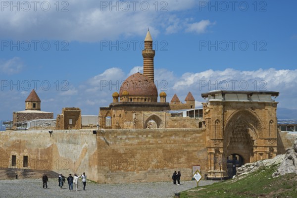 A historic building with a sandstone dome and minaret, surrounded by an old wall, under a blue sky,