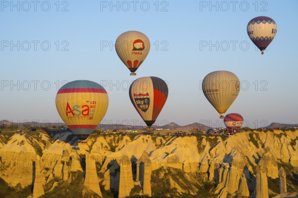 Balloons with logos floating over a rocky landscape with mountain views in the background, hot air