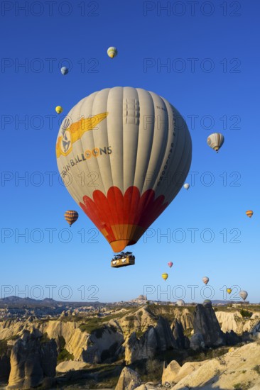 A large colorful balloon with decoration floats over a picturesque rocky landscape, hot air